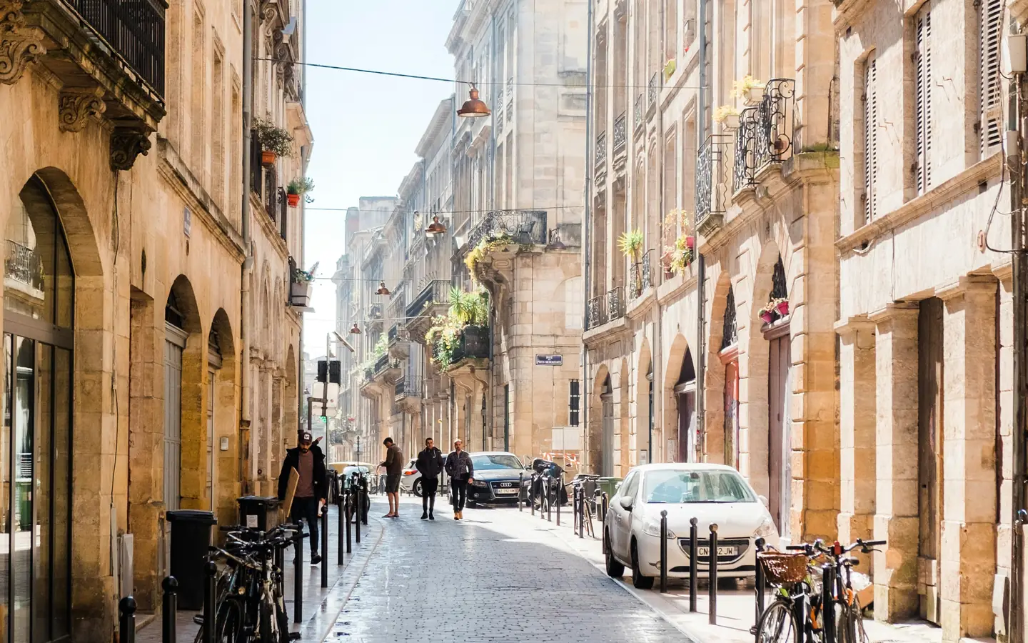 A sunlit French street of stone facades, shutters and iron balconies